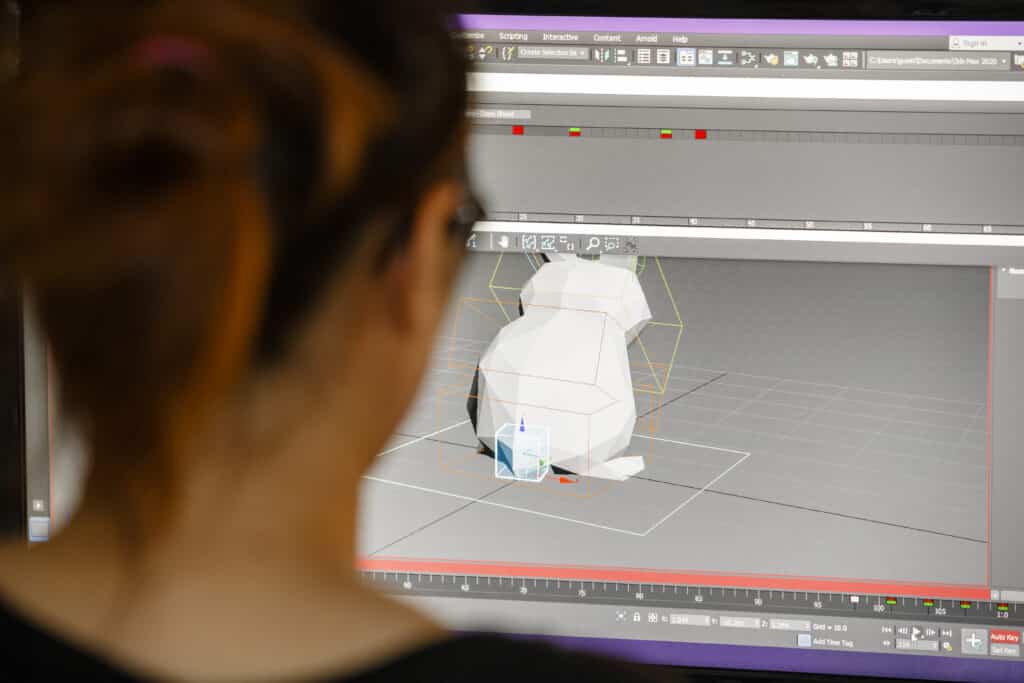 En person tittar på en datorskärm som visar en 3D-modell i ett designprogram. Personen ses bakifrån med fokus på skärmen som visar en polygonmodell i en programvarumiljö.