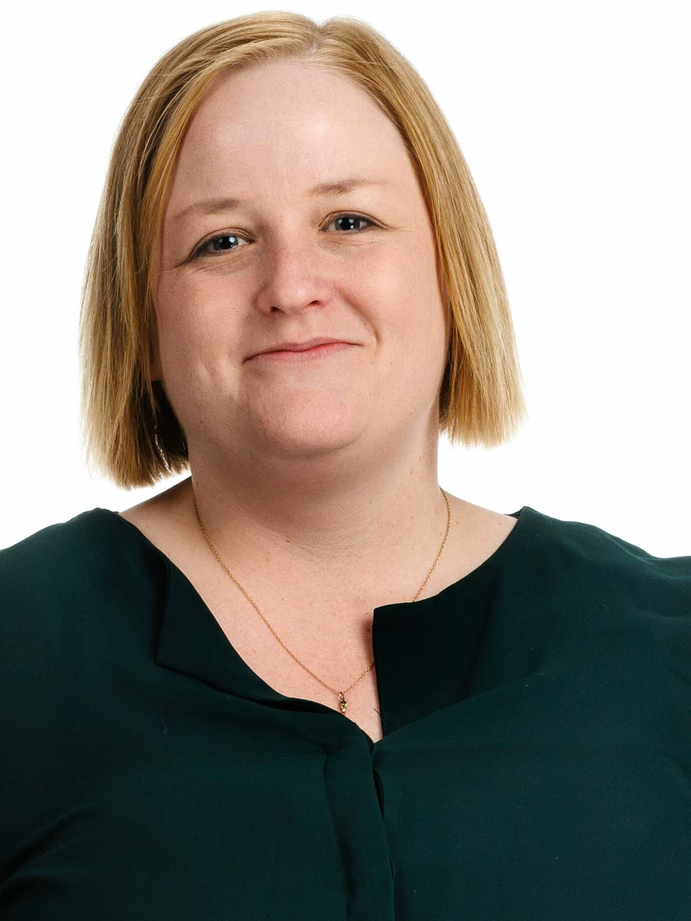 Portrait shot of a woman with blonde hair and a dark green blouse, smiling at the camera.