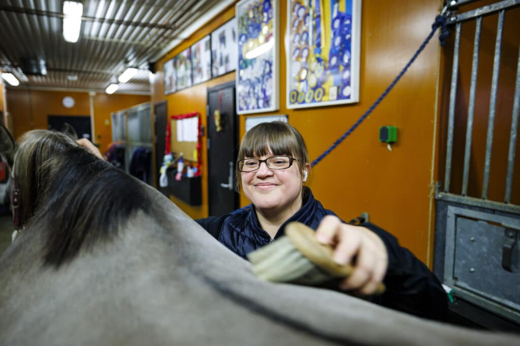 Catrine brushes her horse indoors in the stable