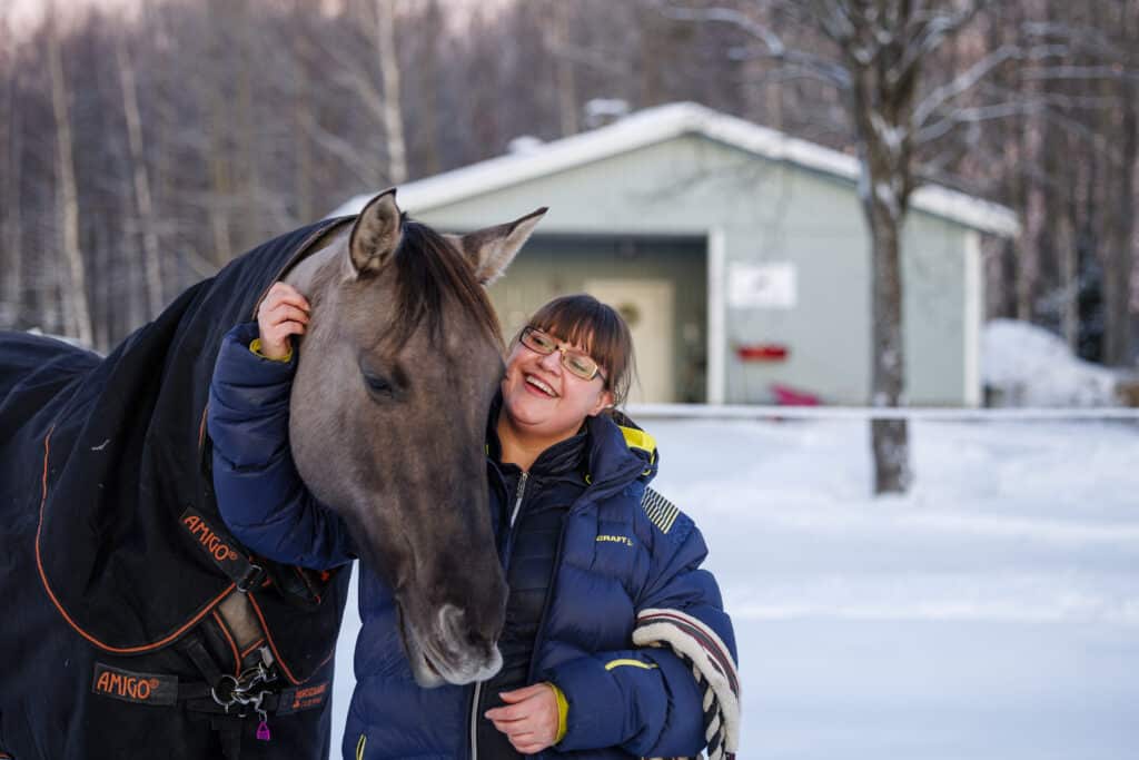 Smiling woman hugs her grey horse outdoors