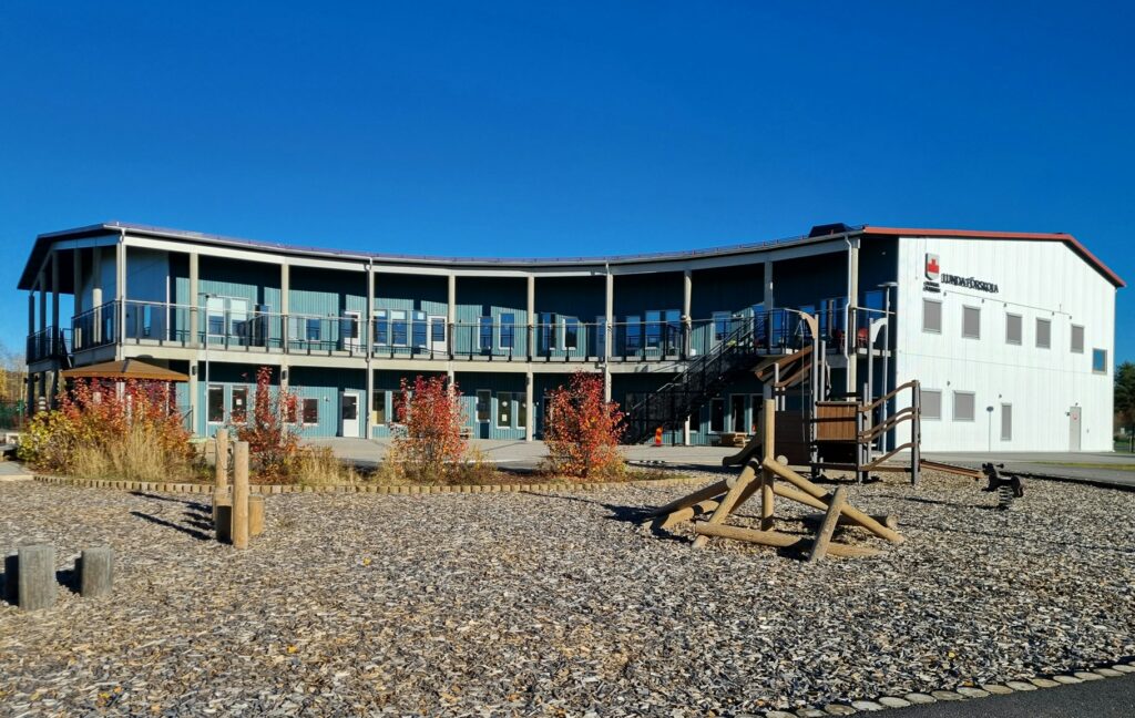 A modern and environmentally friendly preschool building with a curved shape, wooden facade and a playground in the foreground.